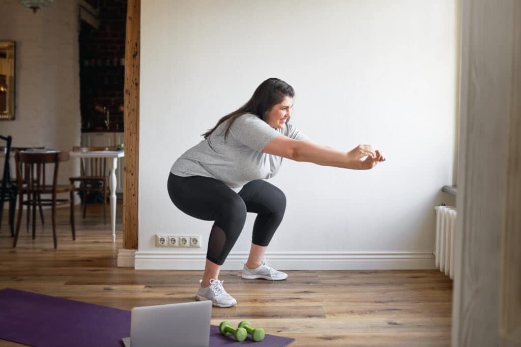 Woman in her home wearing workout clothes and doing squats as part of weight loss routine