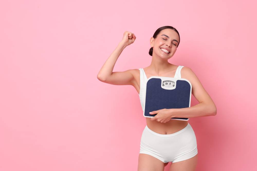 A woman smiling while holding a scale and celebrating after losing weight